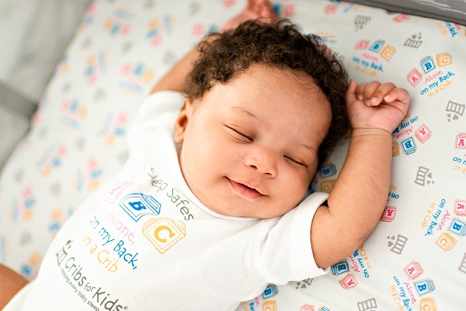 A smiling baby asleep in a safe crib.